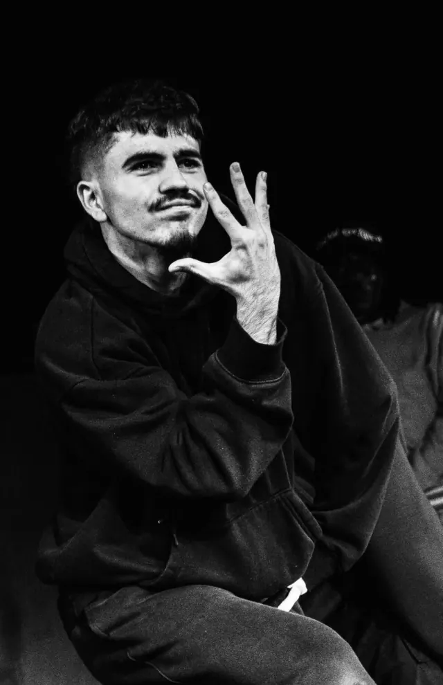 Portrait de PierreDo en sweat noir, la main levée devant le visage, photo en noir et blanc